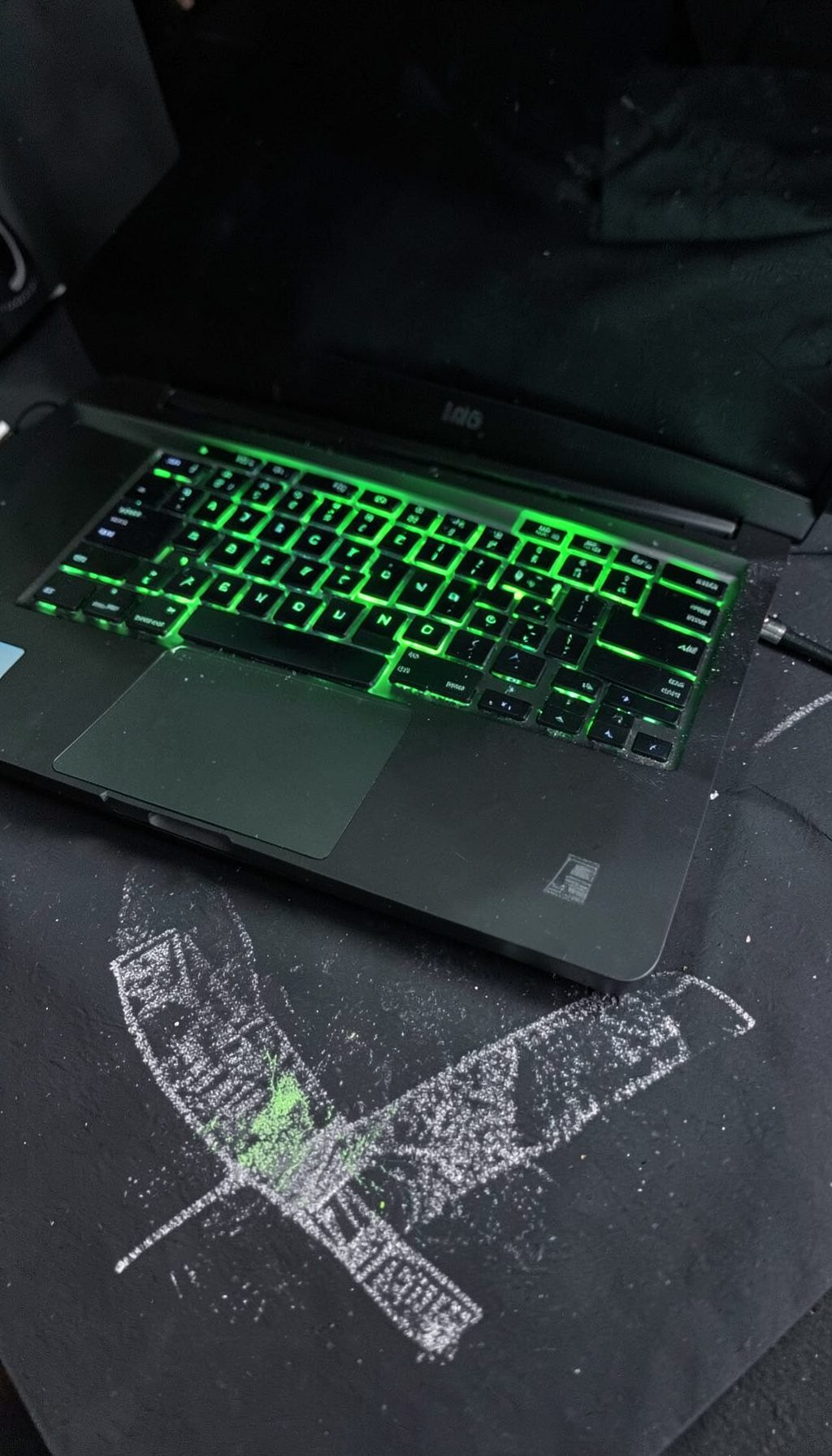 A laptop with a gaming keyboard backlit in green, on a dark desk surface.