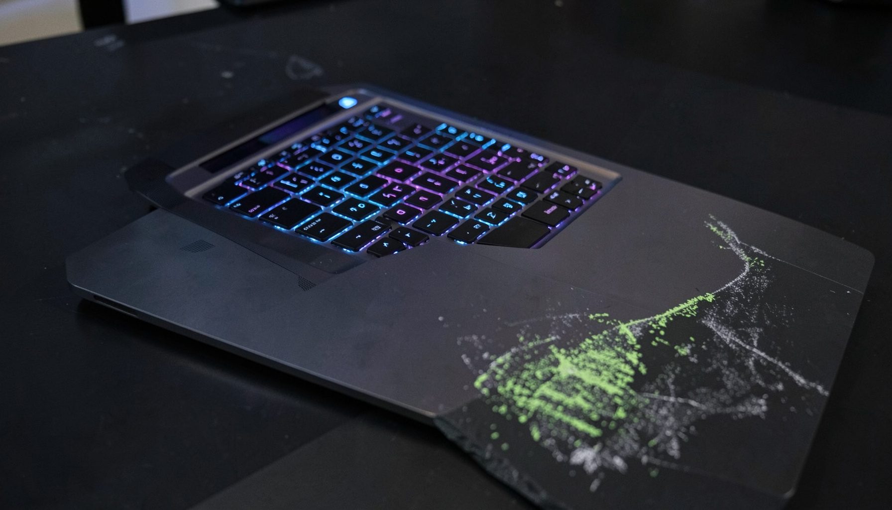 A sleek gaming laptop on a dark desk with subtle RGB keyboard backlighting glowing in blue and purple tones, casting soft reflections on the surface.
